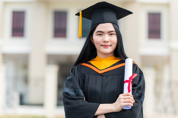 야외에서 졸업 졸업장을 가진 젊은 아시아 여자의 초상화