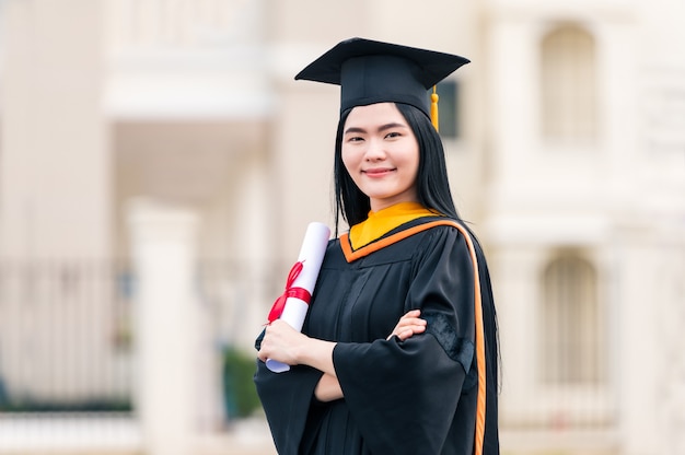 Portrait of young Asian woman with graduation diploma outdoors