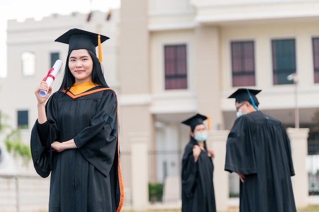 Portrait of young Asian woman with graduation diploma outdoors