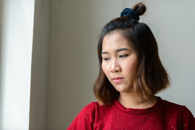 Портрет молодой азиатской женщины с короткими волосами в комнате у окна дома