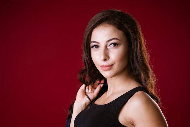 Portrait of a young attractive adult brunette woman with long hair in a black short top on a dark re...