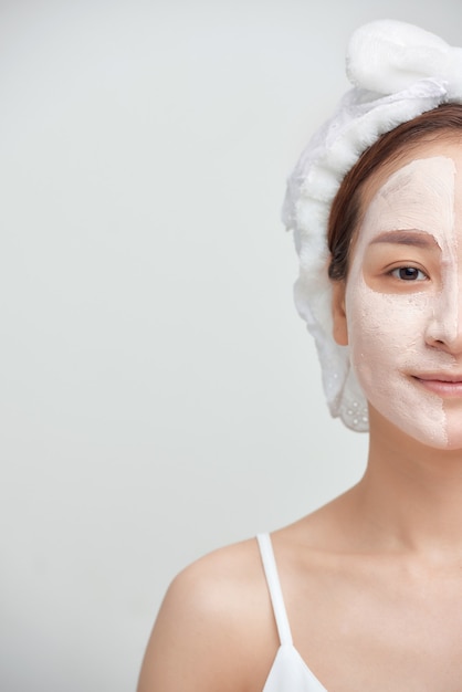 Portrait of young attractive Asian woman with facial clay mask over white background.