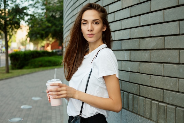 Portrait of a young attractive brunette girl holding milkshake