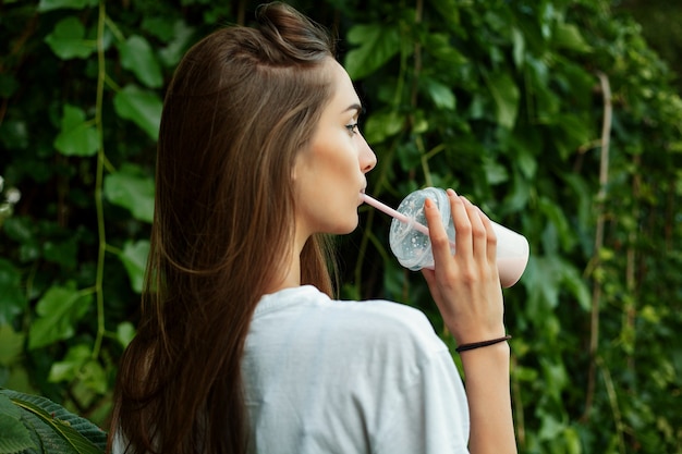 ミルクセーキを飲む白いTシャツの若い魅力的な女性の肖像画