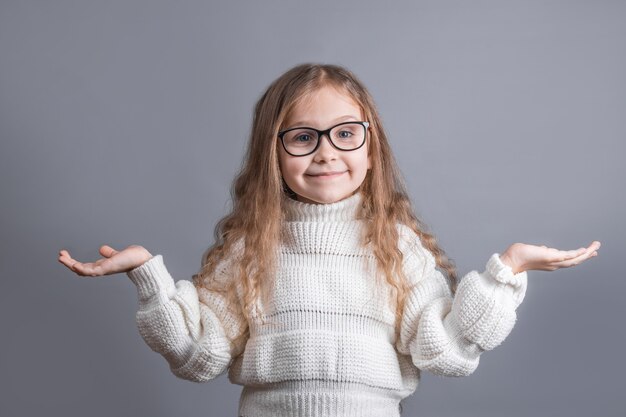 Ritratto di una giovane bambina attraente con capelli biondi in maglione da parte ee si diffonde le mani