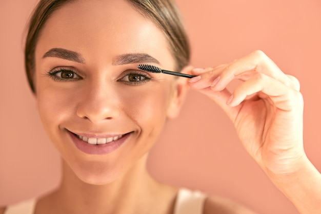 Portrait of a young attractive woman on a beige background
holding a brush for eyebrow and eyelash makeup