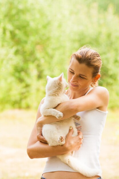 Portrait of young attractive woman holding her white cat and looking into it's eyes, green forest background