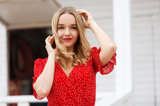 portrait a young attractive woman in red dress with deep neckline outdoors in sunny day. beautiful smiling girl with red lipstick in  short red dress in summer. portrait of happy blonde woman outdoors