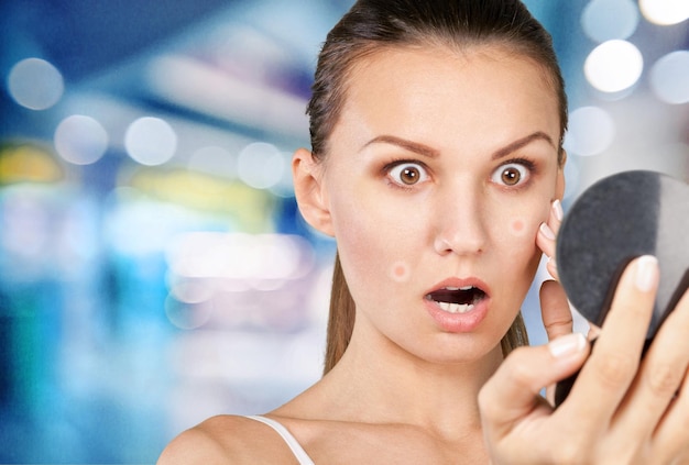 Portrait of young attractive woman touching her face and looking for acne