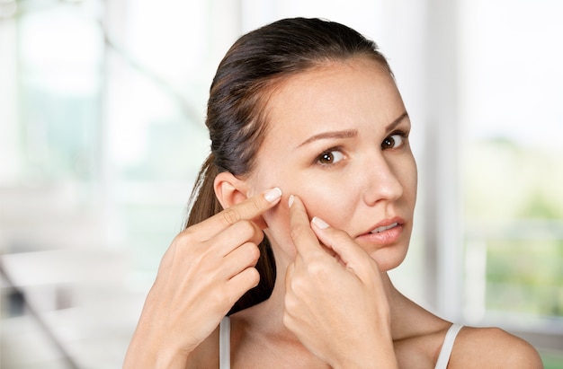 Portrait of young attractive woman touching her face and looking for acne