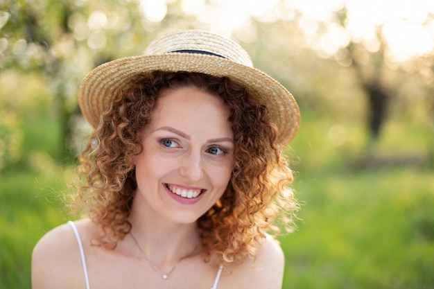 Portrait young attractive woman with curly hair in a stylish wicker hat in a green garden