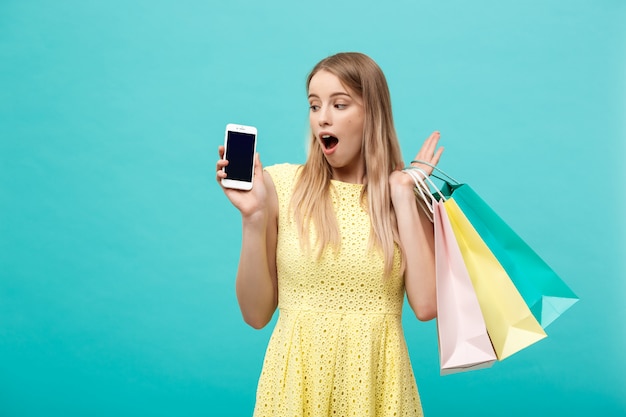 쇼핑백과 세로 젊은 매력적인 여자는 카메라에 직접 휴대 전화의 화면을 보여줍니다.
