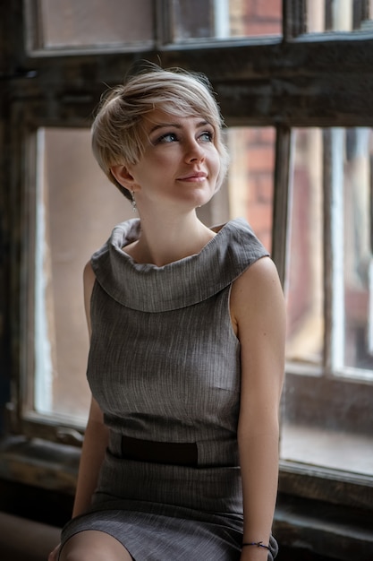 Photo portrait of young attractive woman with short blond hair sitting on the windowsill