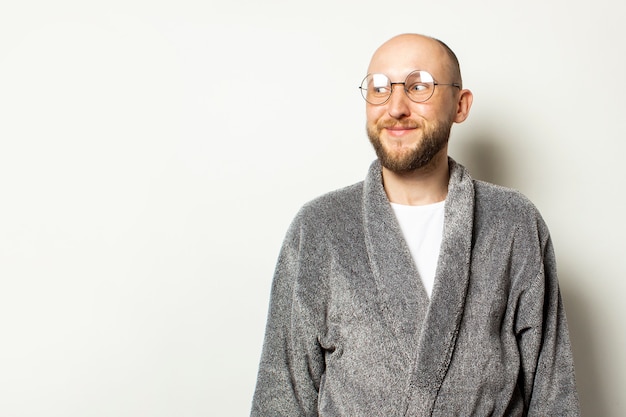 Portrait of a young bald man with a beard in a bathrobe and glasses