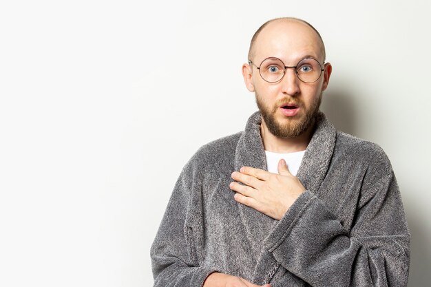 Portrait of a young bald man with a beard in a dressing gown and glasses and a surprised face