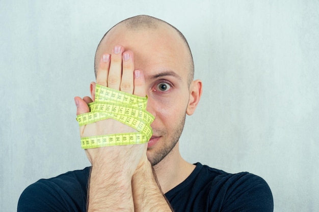 Portrait of a young bald man with hands tied with a measuring tape. concept of diet and anorexia