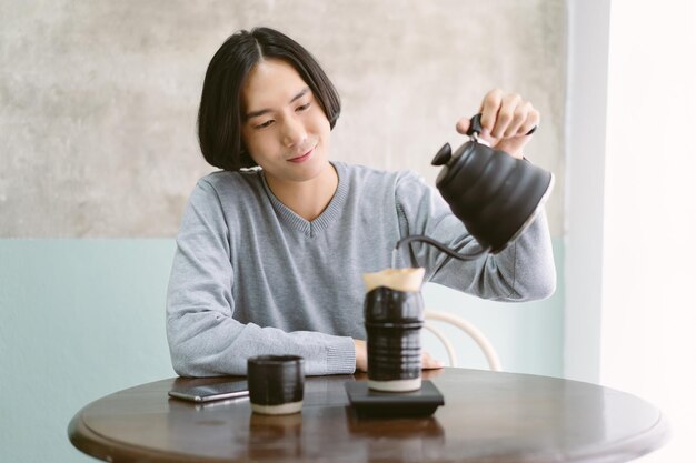 Ritratto di giovane barista uomo asiatico con il sorriso fa il caffè caldo con lo strumento dell'attrezzatura che si prepara al bar al tavolo nella sua casa attività di vacanza e concetto di stile di vita