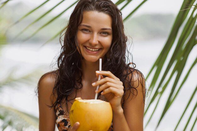 Portrait of Young Beach Woman in a Swimsuit With Fresh Coconut on the Seashore Under a Palm Tree