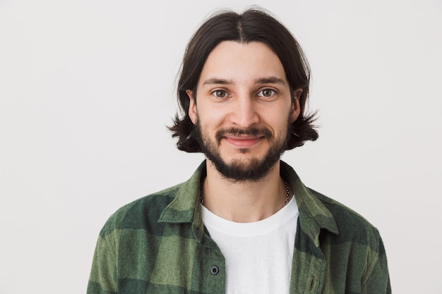 Photo portrait of a young bearded brunette man wearing plaid shirt standing isolated over white wall, smiling