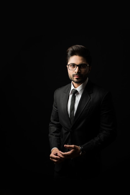 Photo portrait of young bearded indian businessman against black background, moody lighting