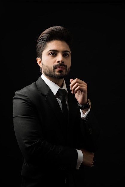 Portrait of young bearded Indian businessman against black background, moody lighting