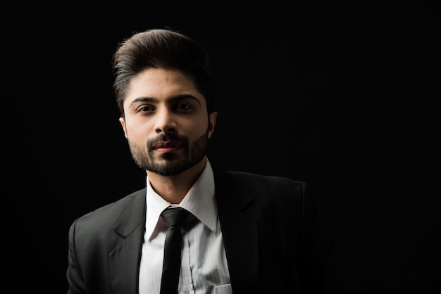 Portrait of young bearded Indian businessman against black background, moody lighting