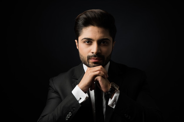 Portrait of young bearded Indian businessman against black background, moody lighting