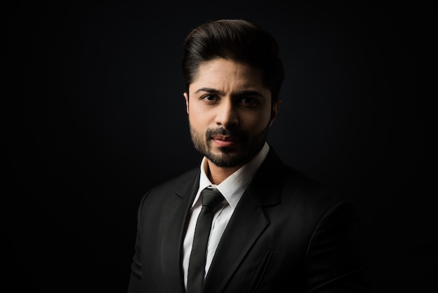 Portrait of young bearded Indian businessman against black background, moody lighting