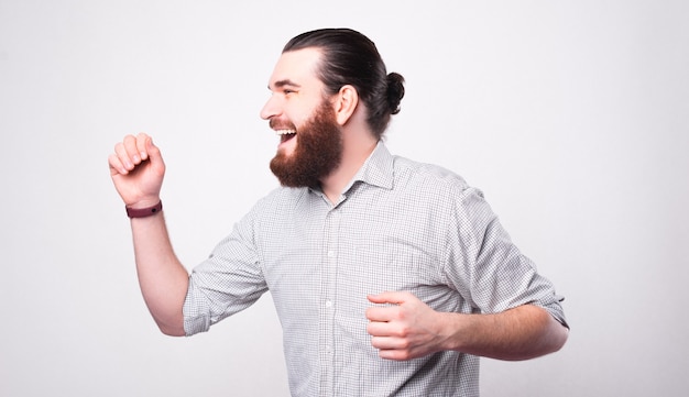 A portrait of a young bearded man being very excited is looking away near a white wall