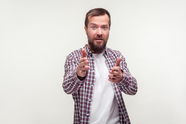 Portrait of young bearded man in casual plaid shirt pointing at camera finger guns with positive face expression pretending to shoot kill threat indoor studio shot isolated on white background