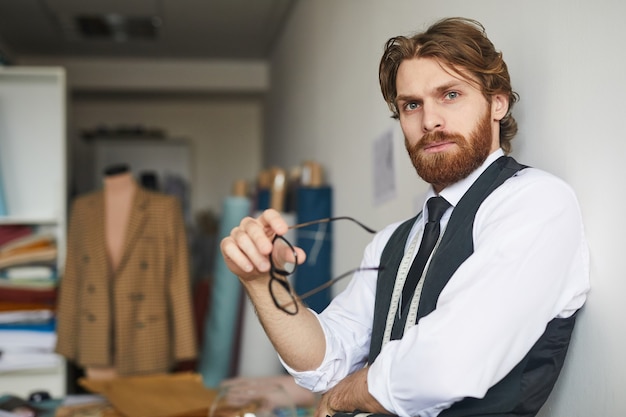 Portrait of young bearded man leaning on the wall and in the workshop