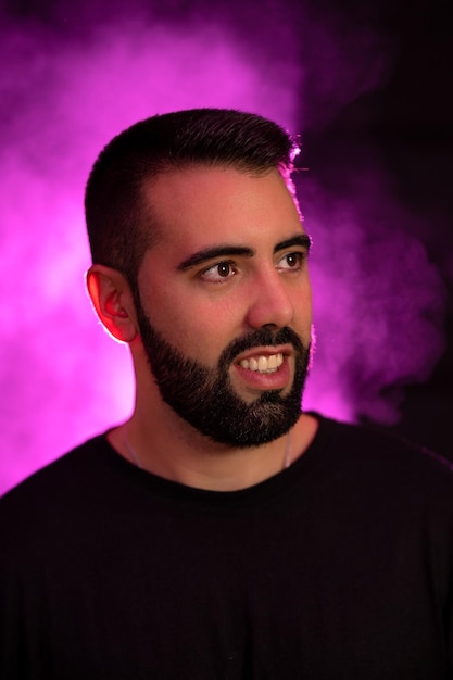 Portrait of a young bearded man on a purple and black background with smoke