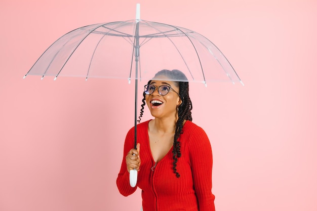 Portrait of young beautiful african american woman holding umbrella isolated on a Pink background