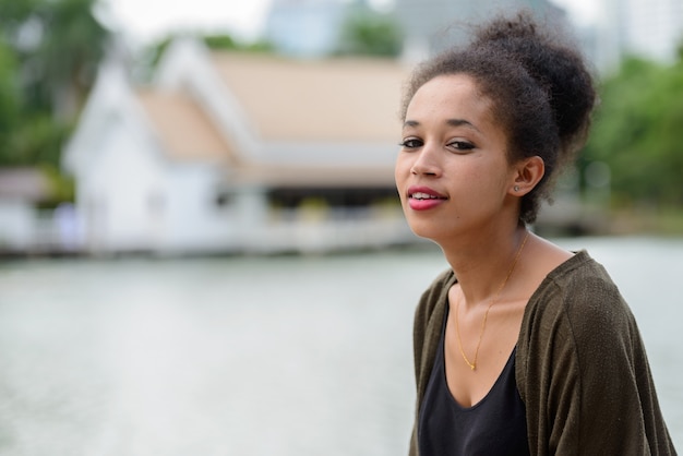 Portrait of young beautiful African woman with Afro hair relaxing at the park outdoors