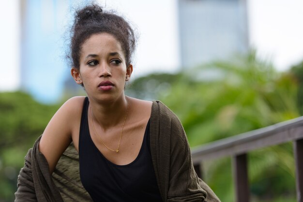 Portrait of young beautiful African woman with Afro hair relaxing at the park outdoors