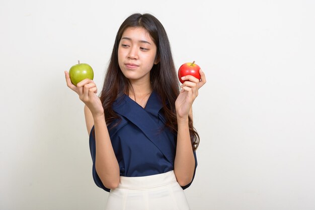 Portrait of young beautiful Asian businesswoman choosing between two apples