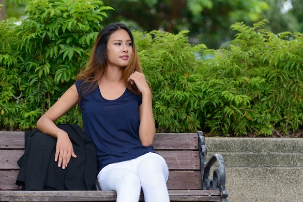 Портрет молодой красивой азиатской бизнес-леди, расслабляющейся в парке на открытом воздухе
