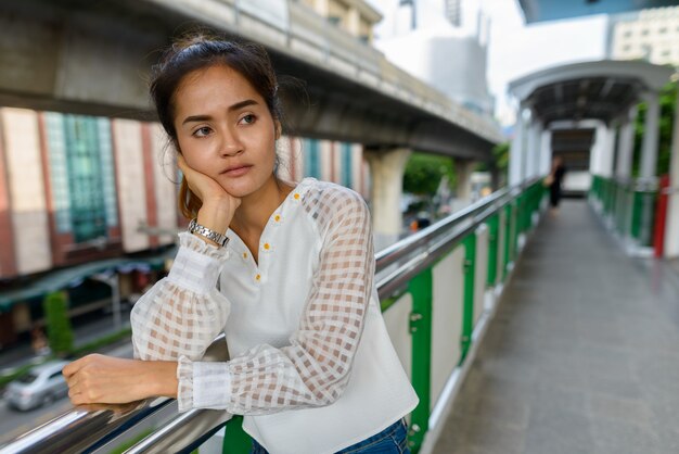 Ritratto di giovane bella donna d'affari asiatica alla stazione del treno del cielo all'aperto della città