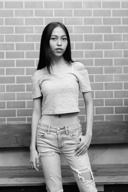 Portrait of young beautiful Asian girl on brick wall outdoors in black and white