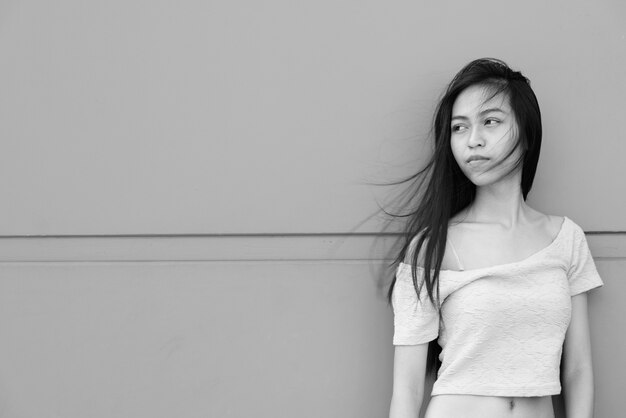 Portrait of young beautiful Asian girl on concrete wall outdoors in black and white