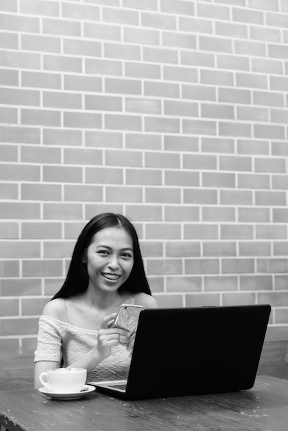 Портрет молодой красивой азиатской девушки, расслабляющейся в кафе на открытом воздухе в черно-белом