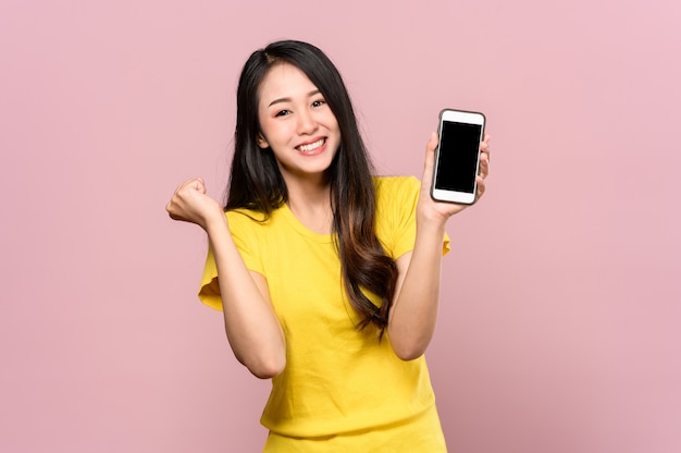 幸せや驚きを感じ、ピンクのスマートフォンを保持している若い美しいアジアの女性の肖像画。