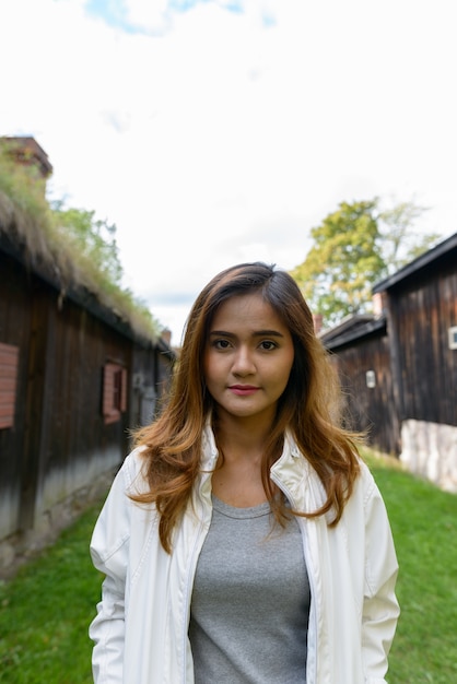 Portrait of young beautiful Asian woman in the middle of aligned old wooden cottages