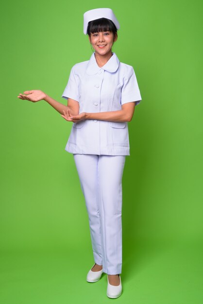 Portrait of young beautiful Asian woman nurse against green wall