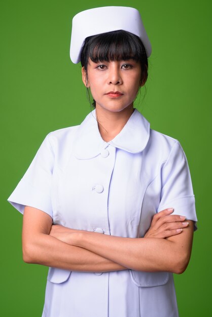 Portrait of young beautiful Asian woman nurse against green wall