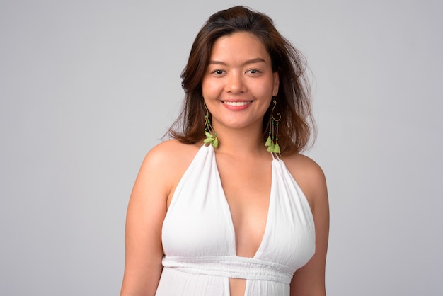 Portrait of young beautiful Asian woman ready for summer against white wall