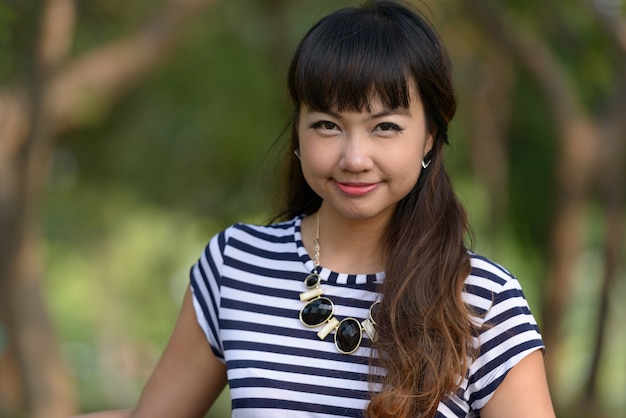 Portrait of young beautiful Asian woman relaxing at the park outdoors