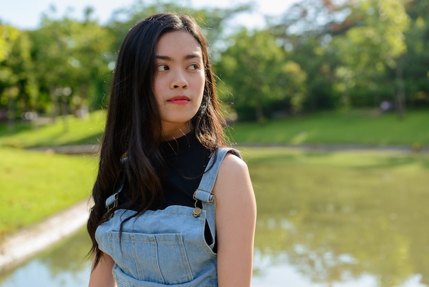 Portrait of young beautiful Asian woman relaxing at the park outdoors