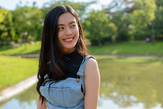 Portrait of young beautiful Asian woman relaxing at the park outdoors