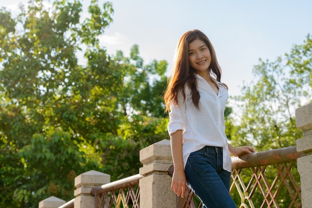 Portrait of young beautiful Asian woman relaxing at the park outdoors